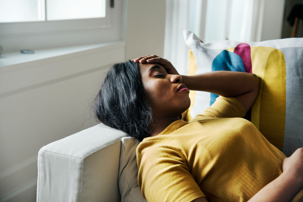 A woman lying on a sofa with one hand on her forehead.